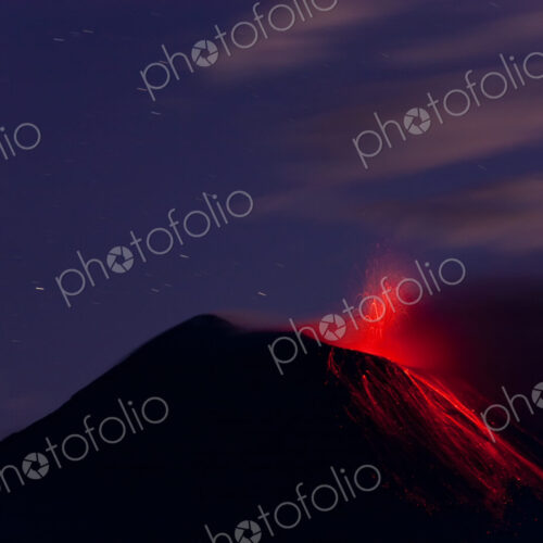 Evening view of fiery eruption of volcano, with lava running down the mountain slopes.