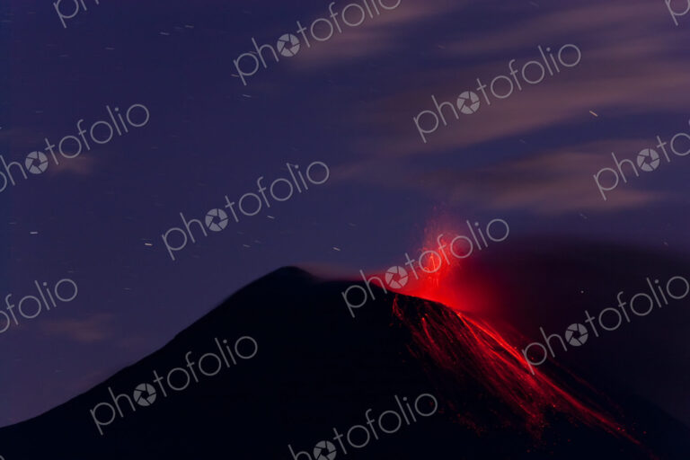Evening view of fiery eruption of volcano, with lava running down the mountain slopes.