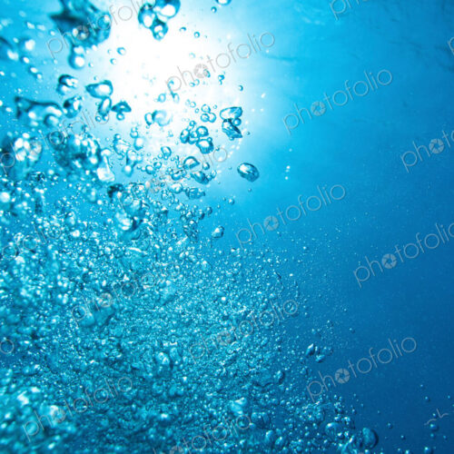 Exhaust bubbles from scuba diver rise towards the surface through water.