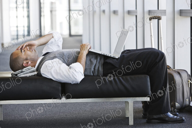 Exhausted businessman taking a short break laying on a bench in an office lobby.