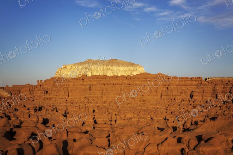 Expansive view of countless hoodoo rock formations under warm evening light, with a…