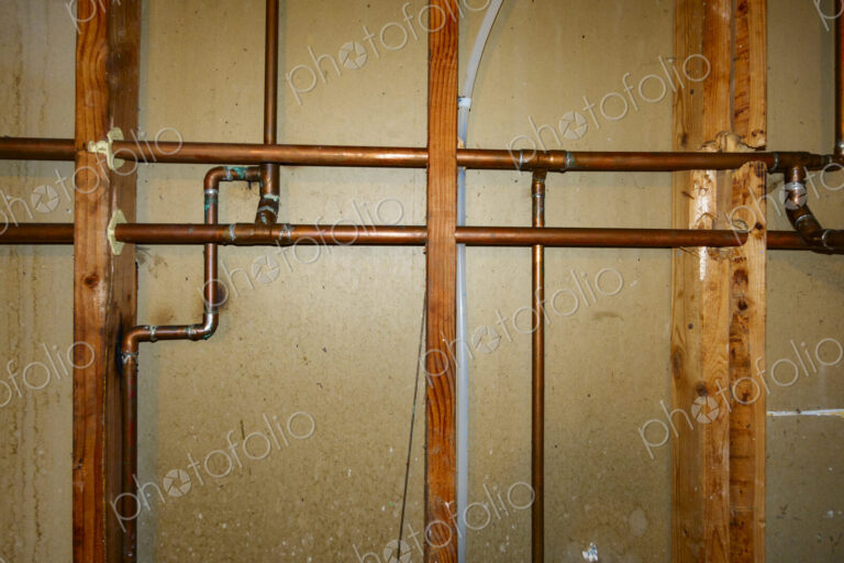 Exposed copper pipes in a network on a wall.