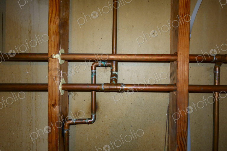 Exposed copper pipes in a network on a wall.