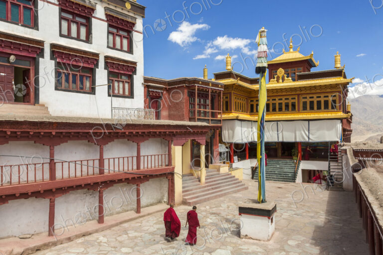 Exterior view of Buddhist monastery with two monks walking across courtyard.
