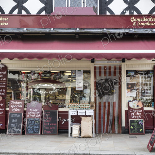 Exterior view of a butcher shop with red awning, blackboards on pavement advertising…