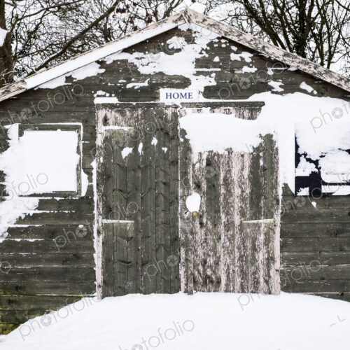 Exterior view of a grey wooden garden shed with snow-covered windows.