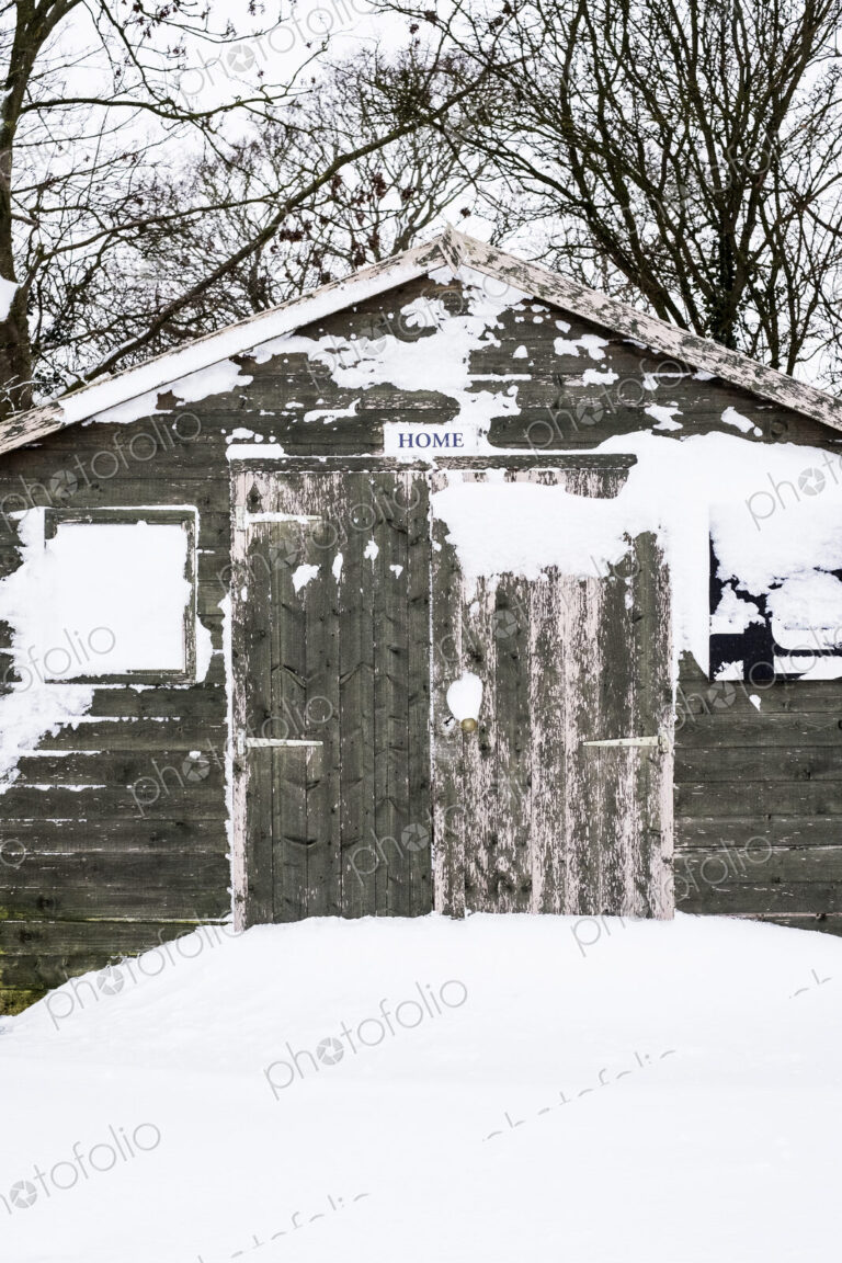 Exterior view of a grey wooden garden shed with snow-covered windows.