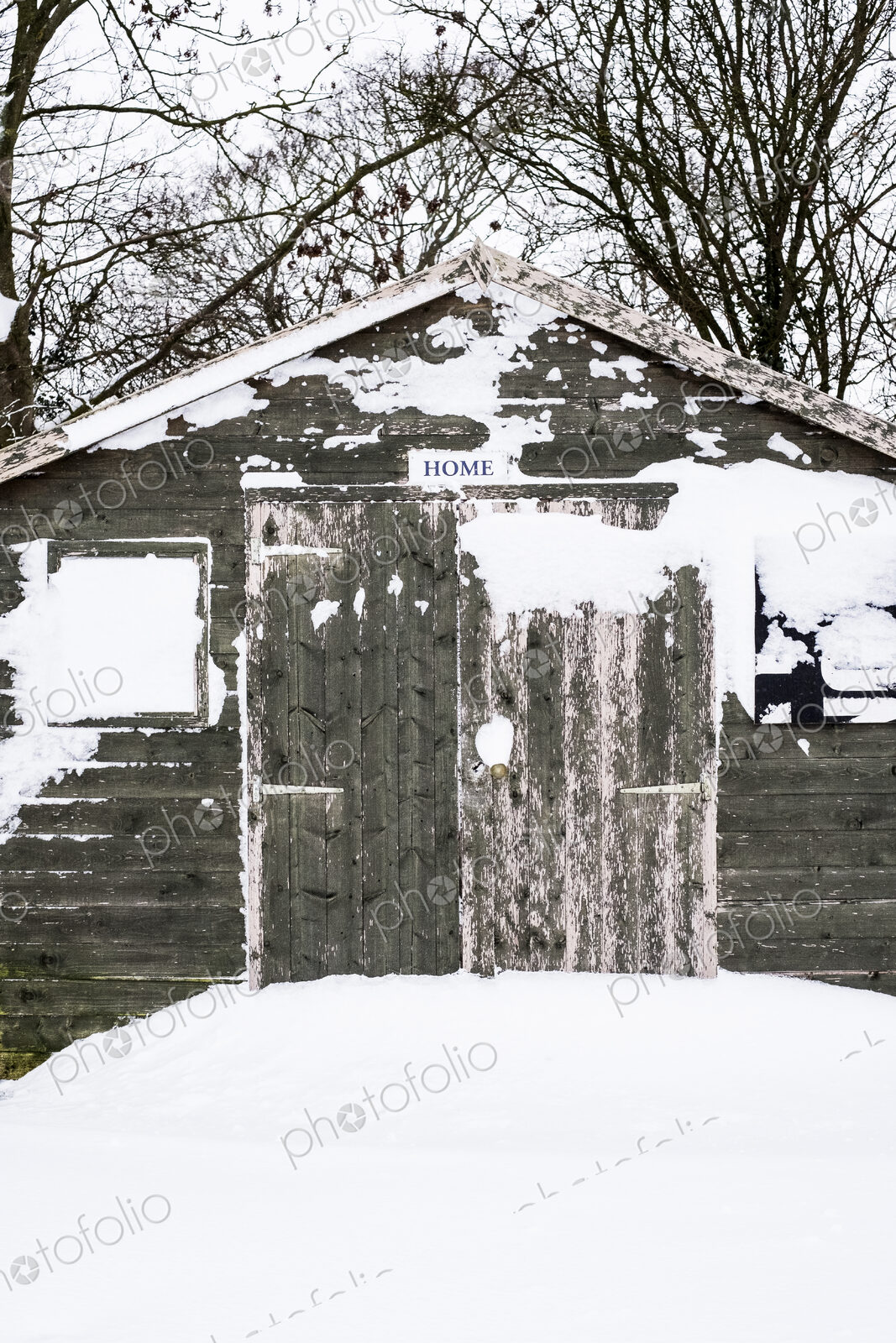 Exterior view of a grey wooden garden shed with snow-covered windows.