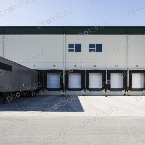 Exterior view of a warehouse loading dock with a truck trailer pulled up to one of the…