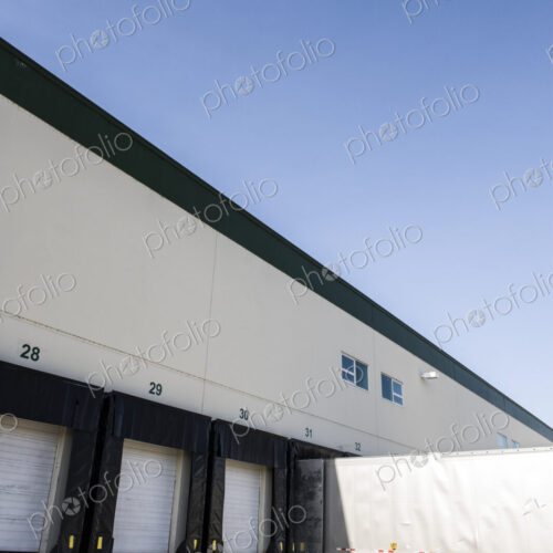 Exterior view of a warehouse loading dock with a truck trailer pulled up to one of the…
