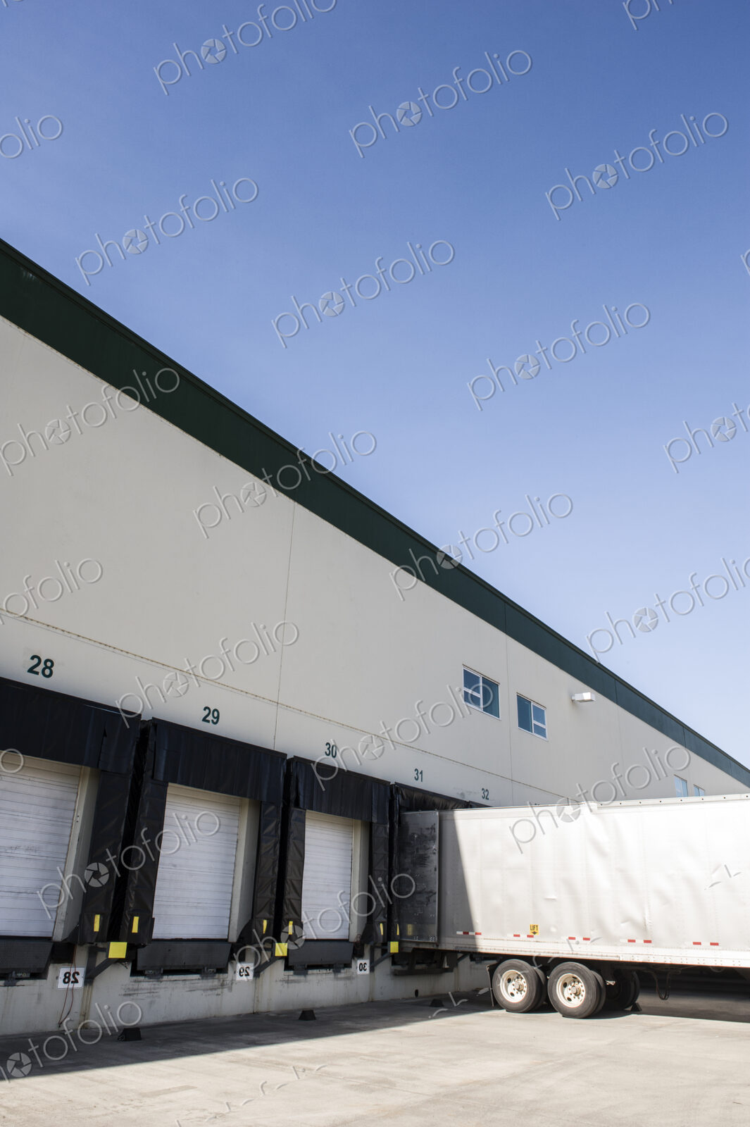 Exterior view of a warehouse loading dock with a truck trailer pulled up to one of the…