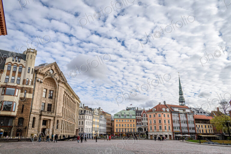 Exterior view of historic buildings in Riga, in a city square under a dramatic cloudy sky.