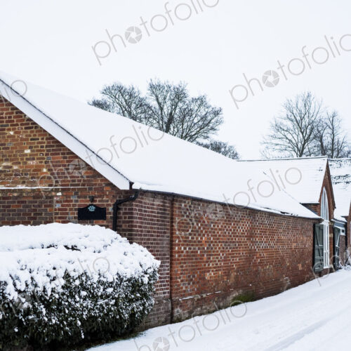 Exterior view of red brick cottages with snow-covered roofs along a rural road.