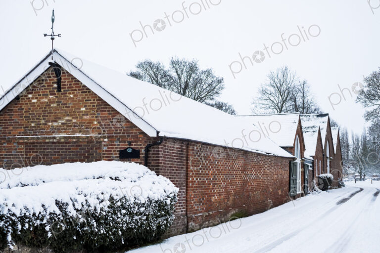 Exterior view of red brick cottages with snow-covered roofs along a rural road.