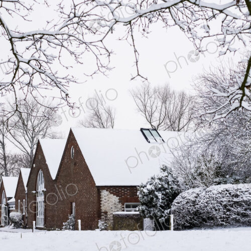 Exterior view of red brick cottages with snow-covered roofs along a rural road.