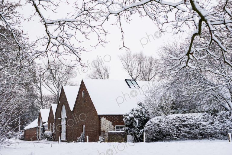 Exterior view of red brick cottages with snow-covered roofs along a rural road.