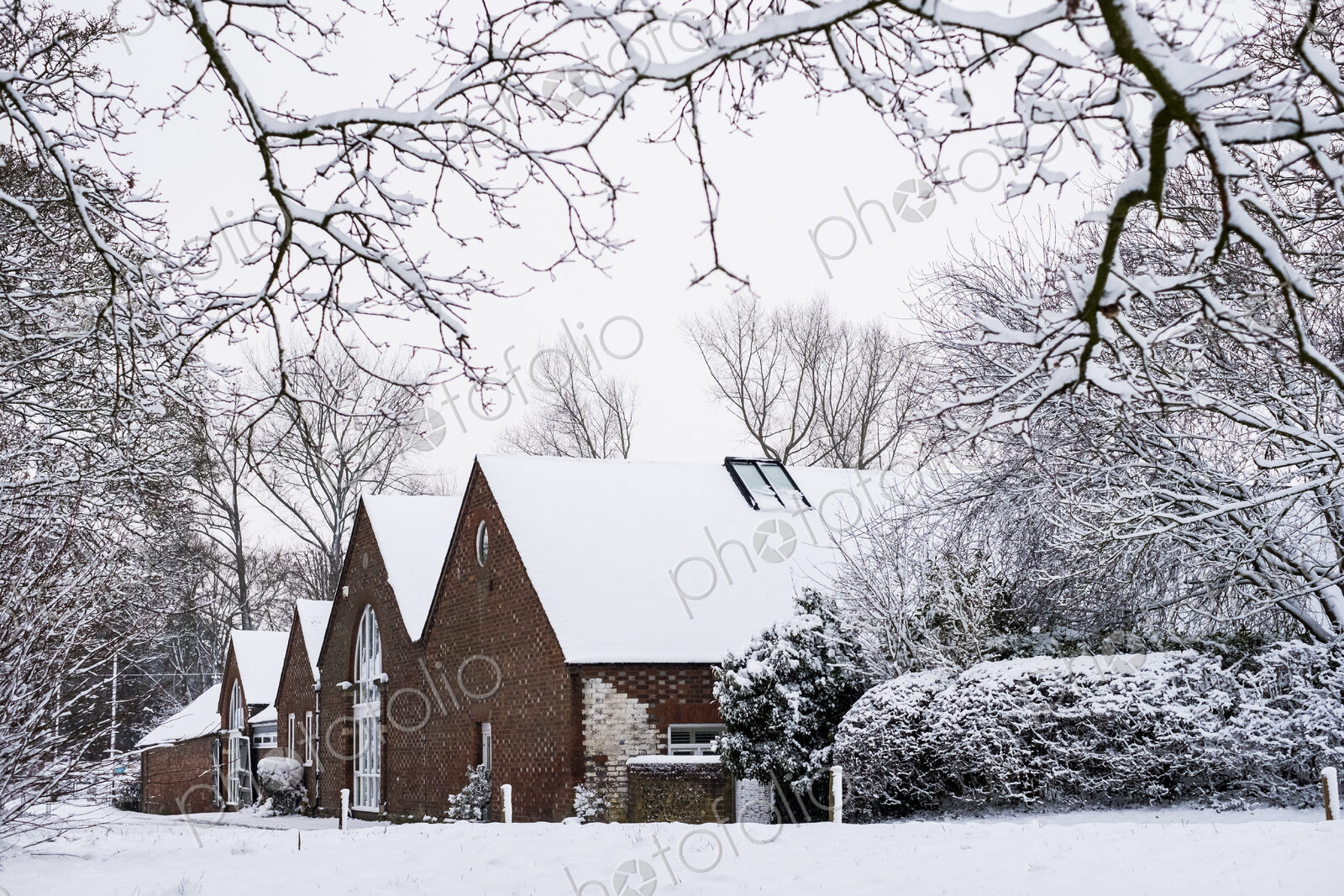 Exterior view of red brick cottages with snow-covered roofs along a rural road.