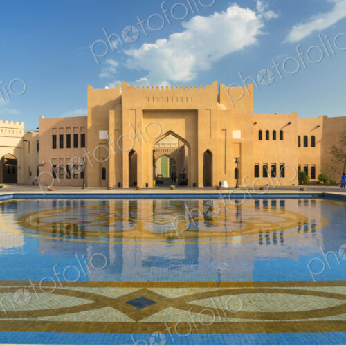 Facade of Middle Eastern building, pond with blue and golden mosaic tiles in foreground. Facade of Middle Eastern building, pond with blue and golden mosaic tiles in foreground.