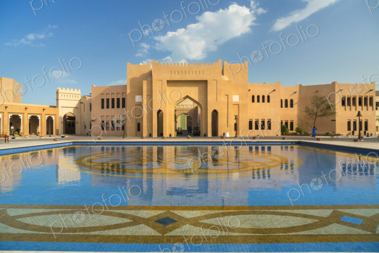 Facade of Middle Eastern building, pond with blue and golden mosaic tiles in foreground.