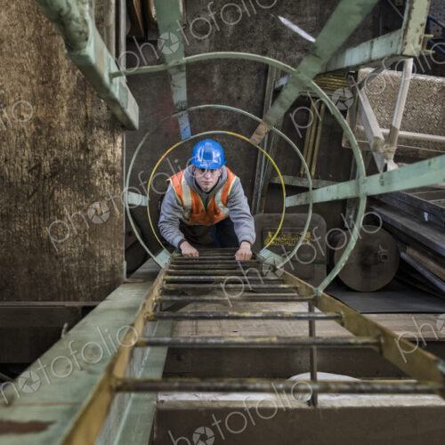 Factory worker climbing up a ladder in a sheet metal factory.