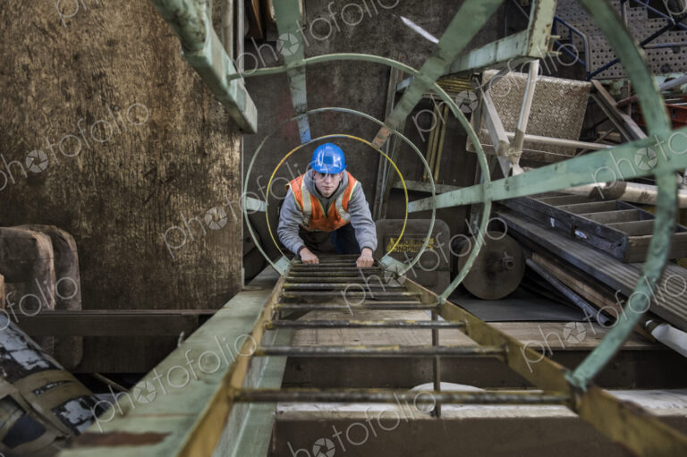 Factory worker climbing up a ladder in a sheet metal factory.