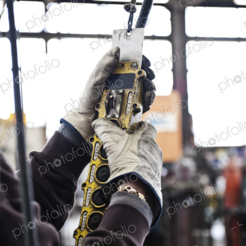 Factory worker using an overhead lift control unit to raise steel pipes in a sheet…