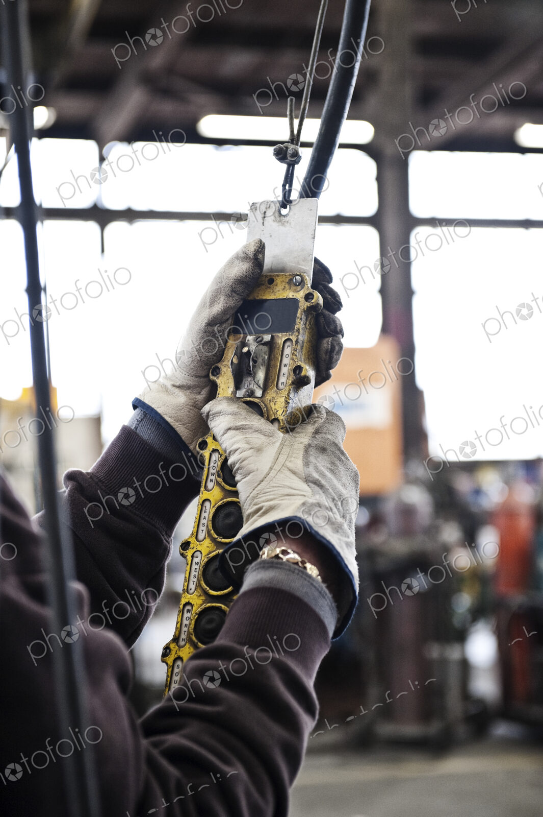 Factory worker using an overhead lift control unit to raise steel pipes in a sheet…