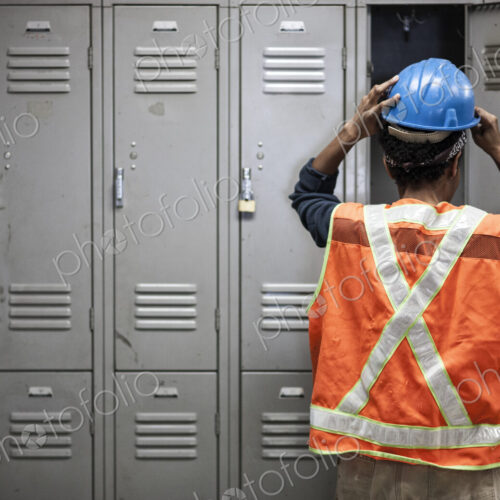 Factory worker wearing a safety vest getting ready for work next to locker in the…