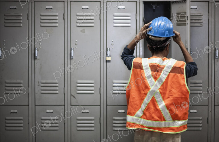 Factory worker wearing a safety vest getting ready for work next to locker in the…