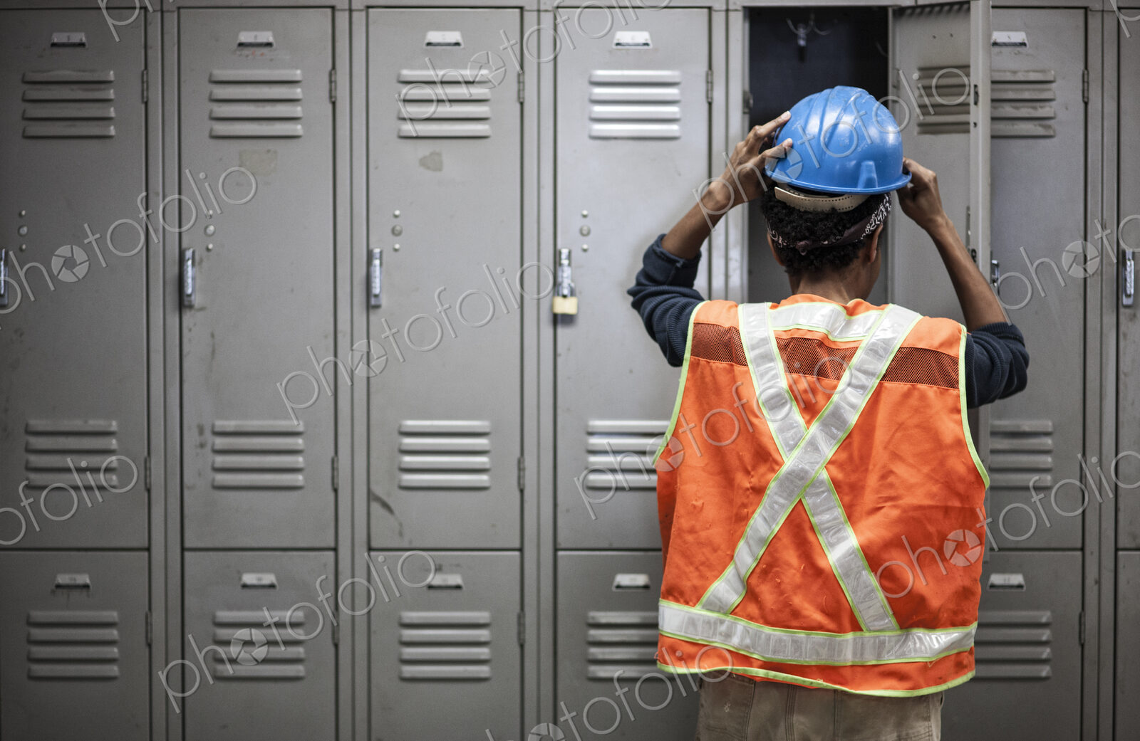 Factory worker wearing a safety vest getting ready for work next to locker in the…