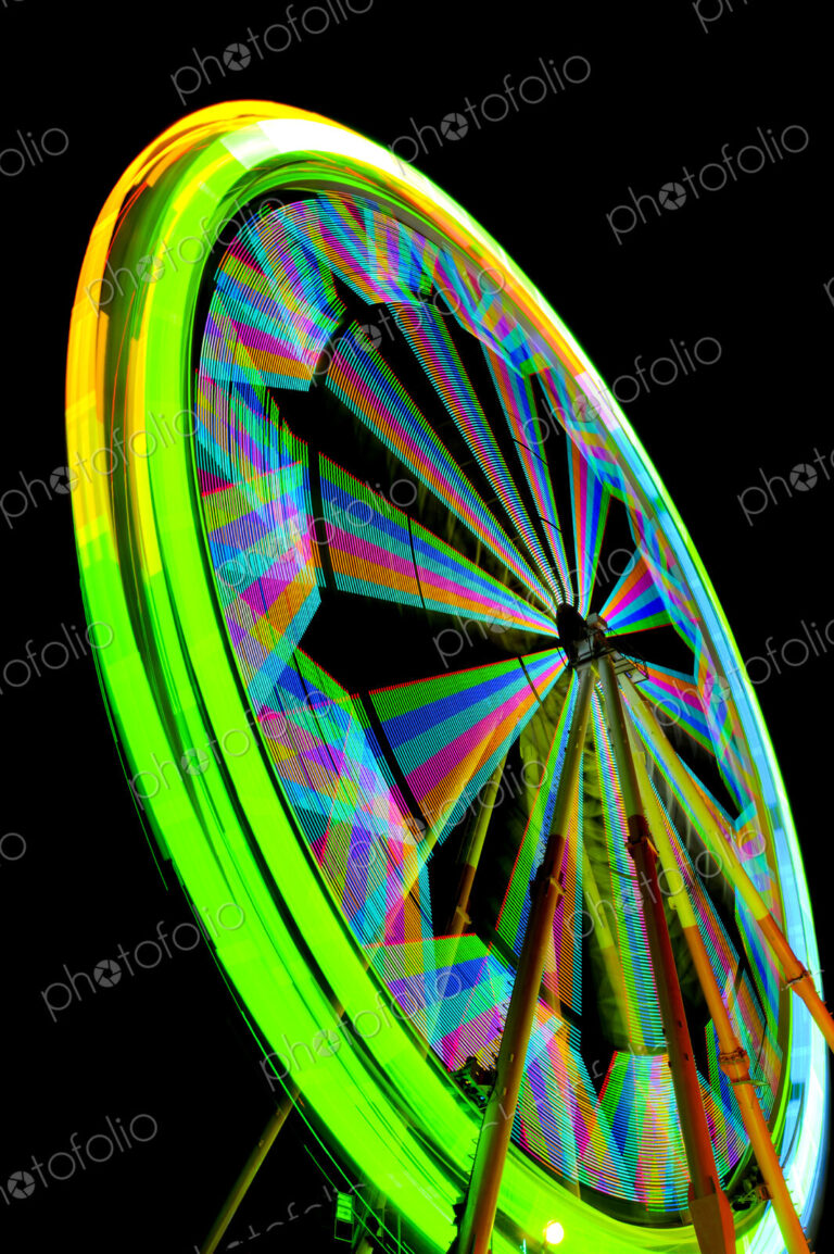 Fairground ferrish wheel with lights in rainbow colours, against a black sky.