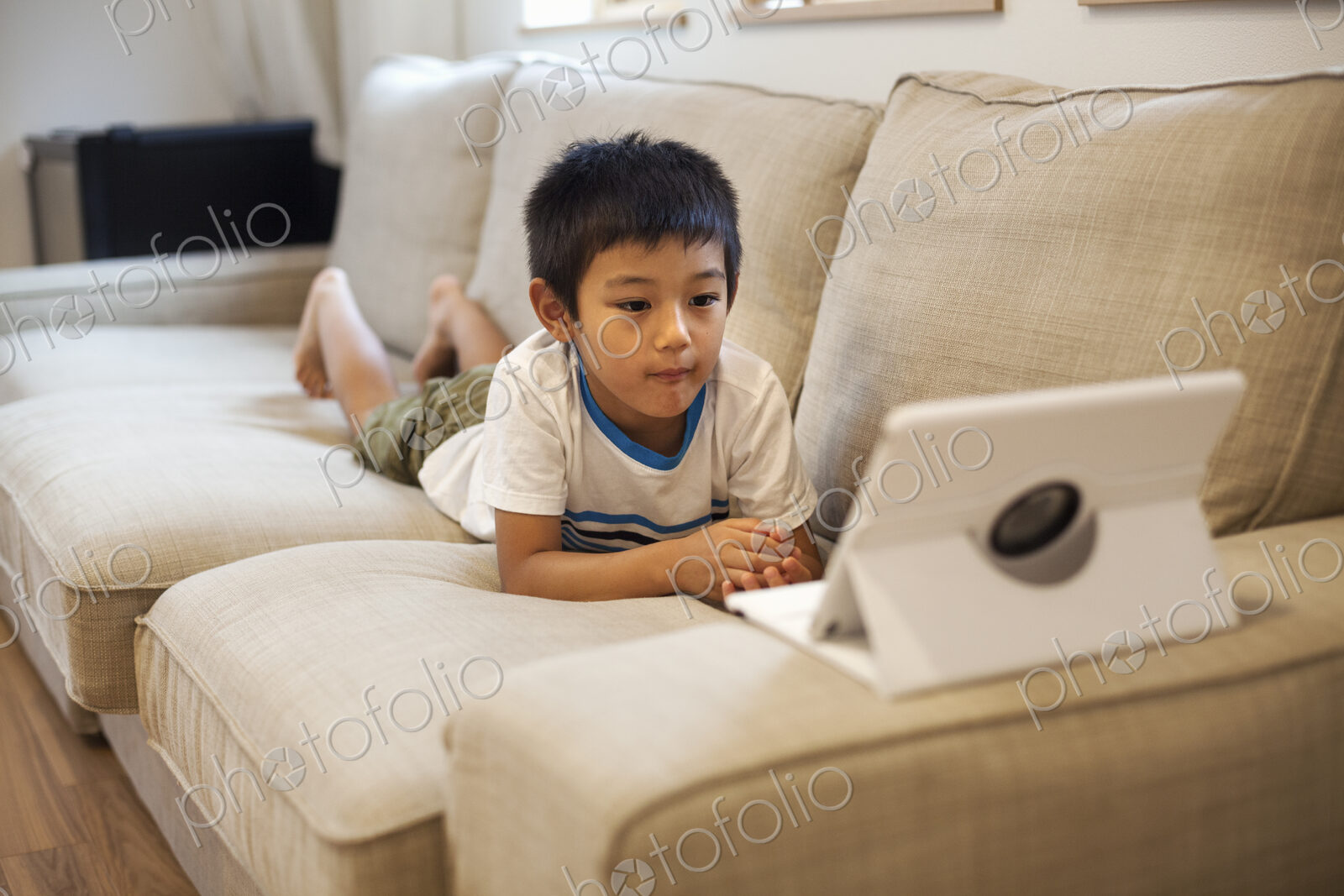 Family home. A boy lying on a sofa watching a digital tablet.