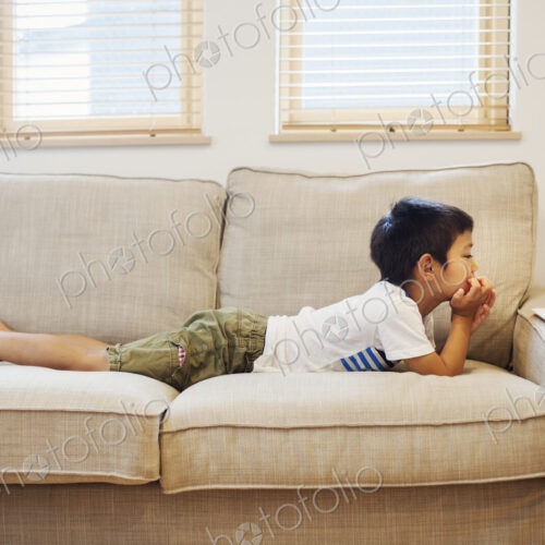 Family home. A boy lying on a sofa watching a digital tablet.