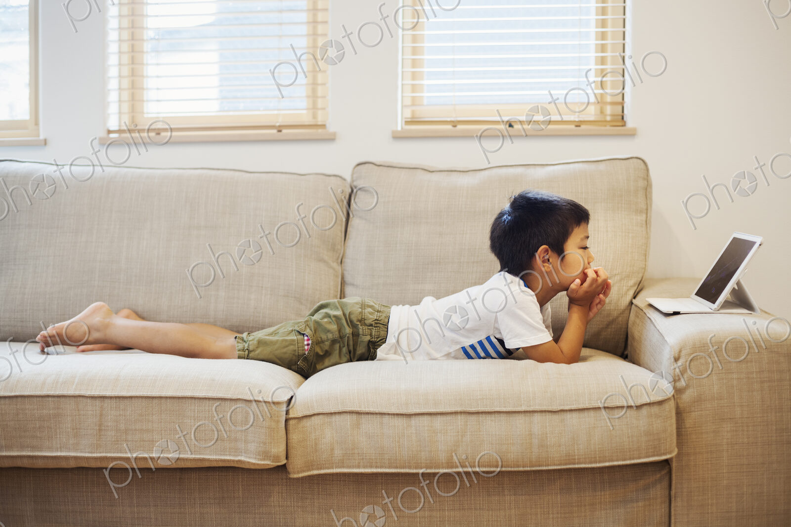 Family home. A boy lying on a sofa watching a digital tablet.