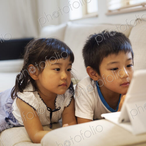 Family home. A boyand a girl lying on a sofa watching a digital tablet.