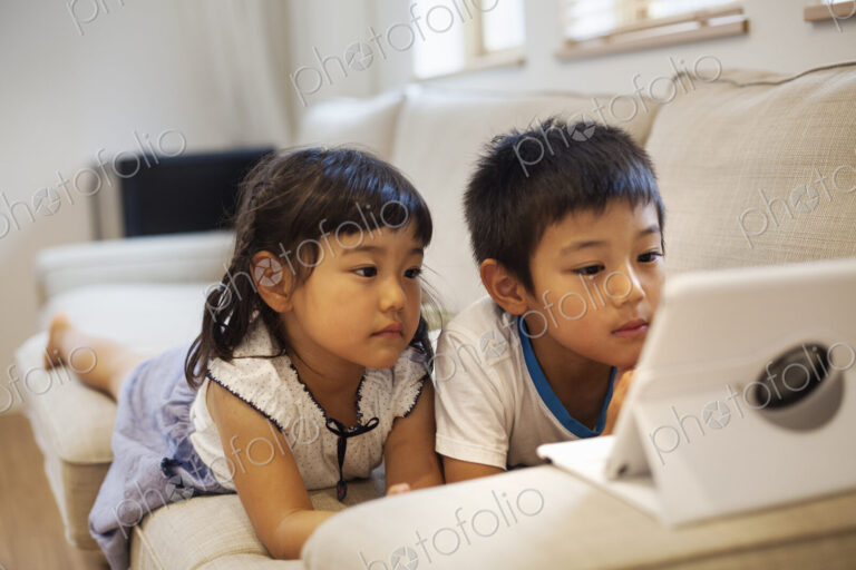 Family home. A boyand a girl lying on a sofa watching a digital tablet.