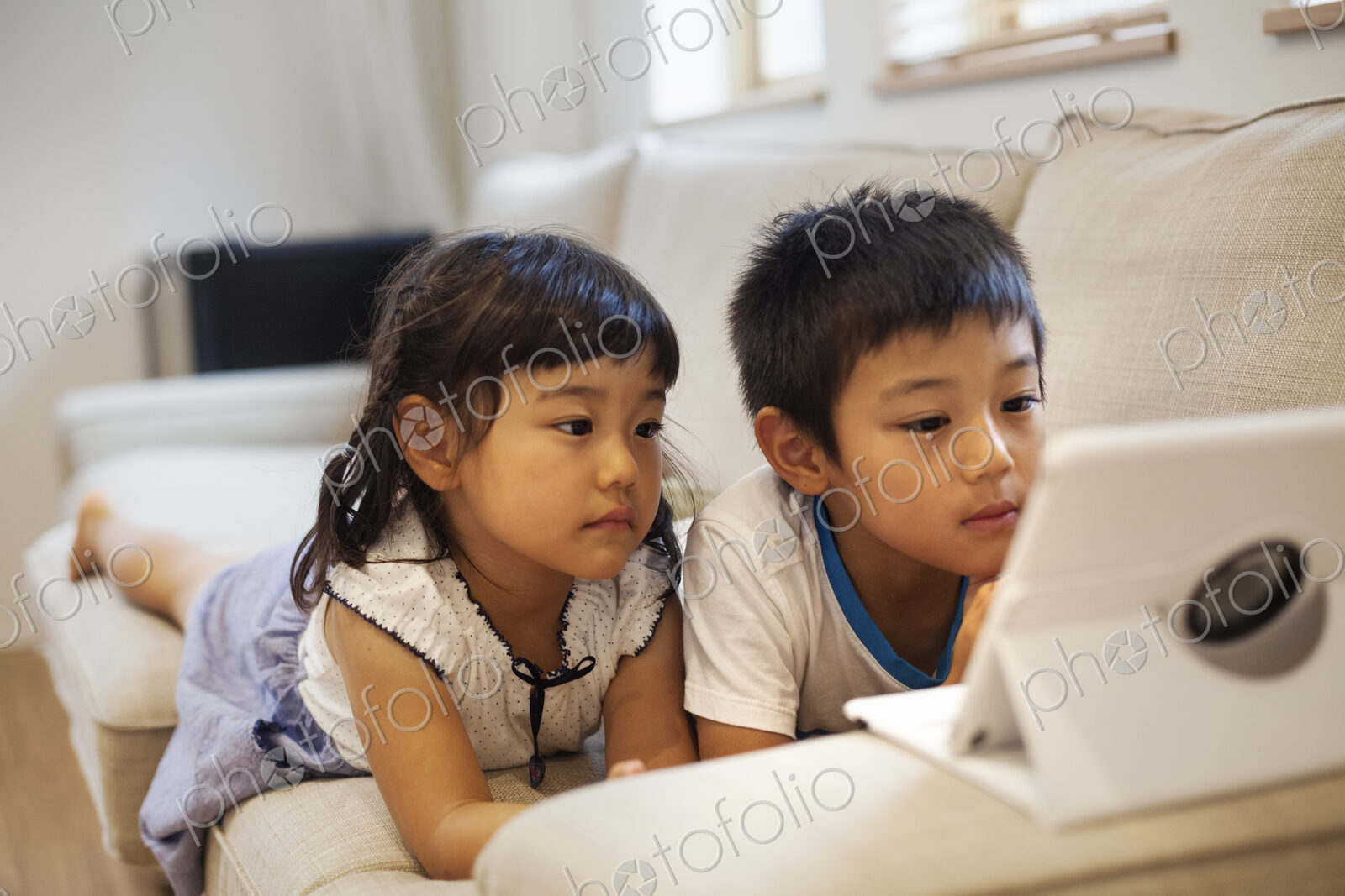 Family home. A boyand a girl lying on a sofa watching a digital tablet.