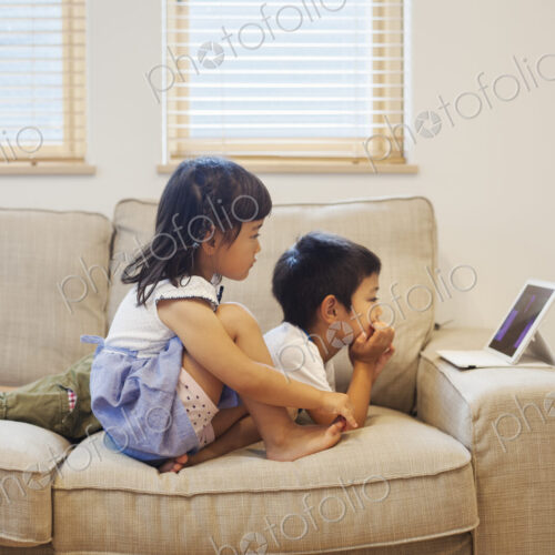 Family home. A boyand a girl lying on a sofa watching a digital tablet.