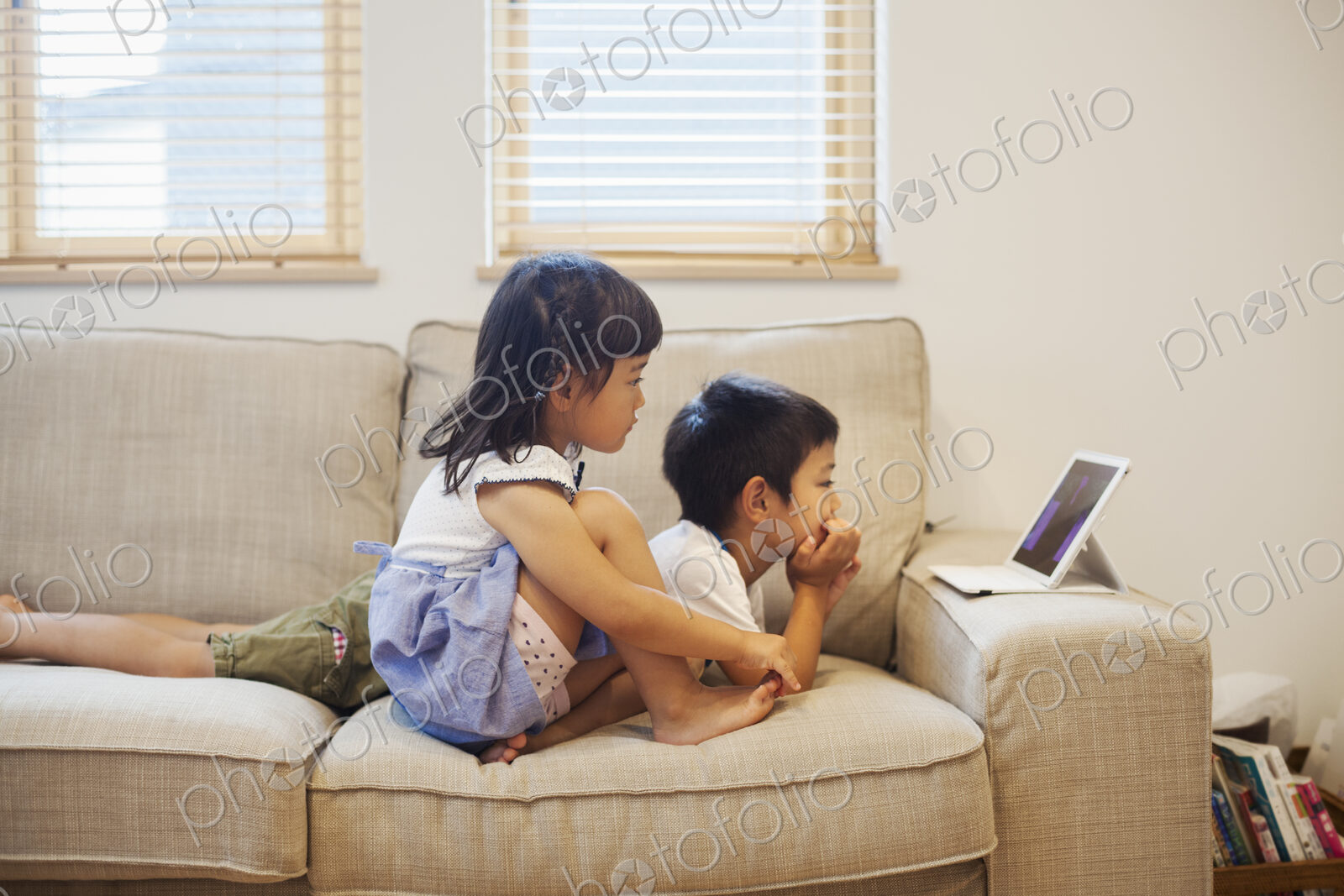 Family home. A boyand a girl lying on a sofa watching a digital tablet.