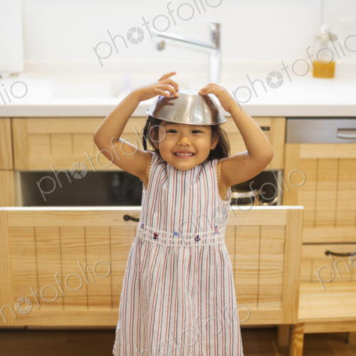 Family home. A child playing, with a metal bowl on her head.