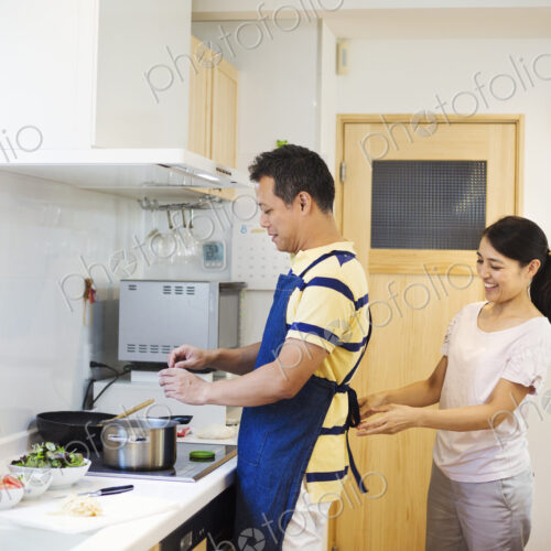 Family home. A man and woman, a wife tying her husband's apron in their kitchen. Family home. A man and woman, a wife tying her husband's apron in their kitchen.