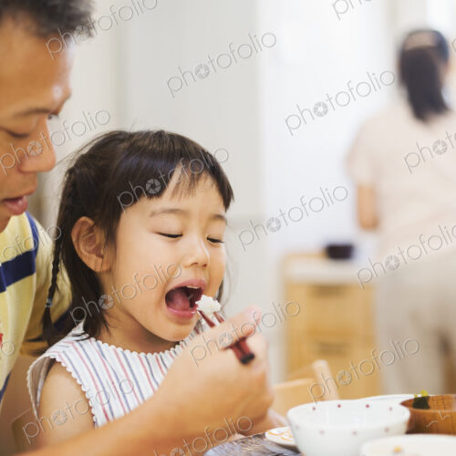 Family home. A man feeding his daughter at a meal. Family home. A man feeding his daughter at a meal.