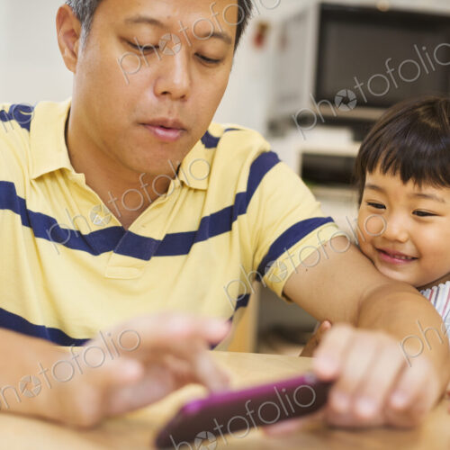 Family home. A man using a smart phone, his daughter beside him.
