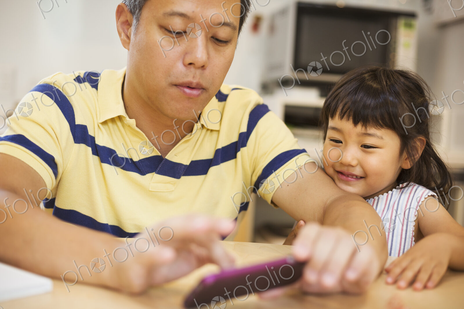 Family home. A man using a smart phone, his daughter beside him.