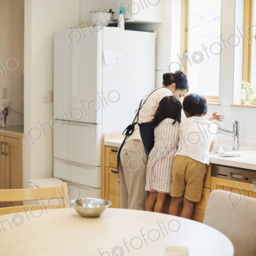 Family home. A mother and two children standing at the sink in a kitchen. Family home. A mother and two children standing at the sink in a kitchen.