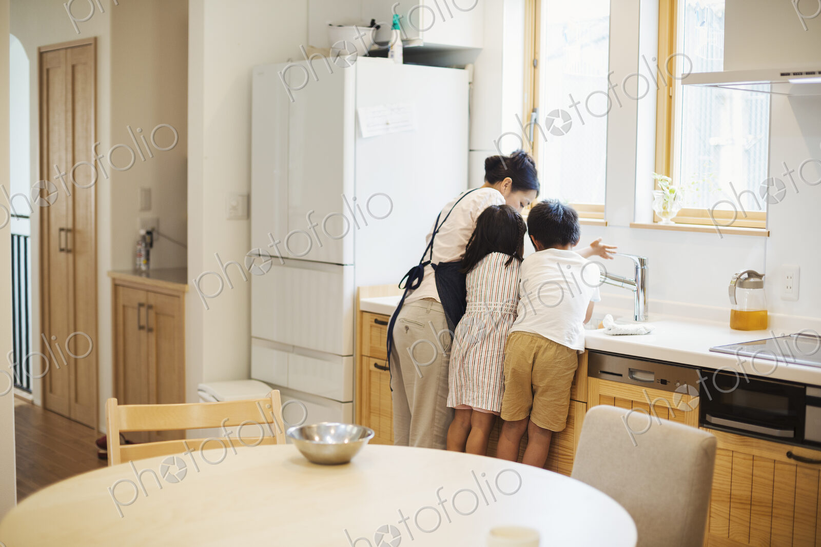 Family home. A mother and two children standing at the sink in a kitchen.
