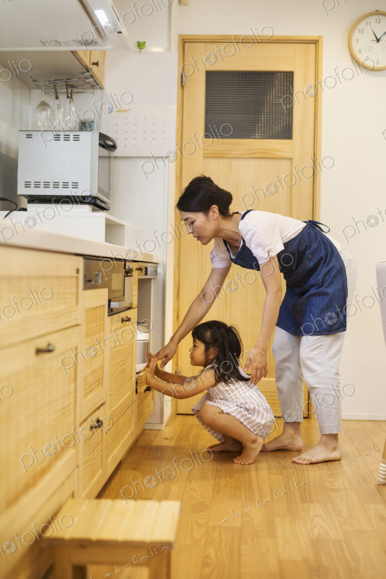 Family home. A woman and a girl bending down to look in an oven.