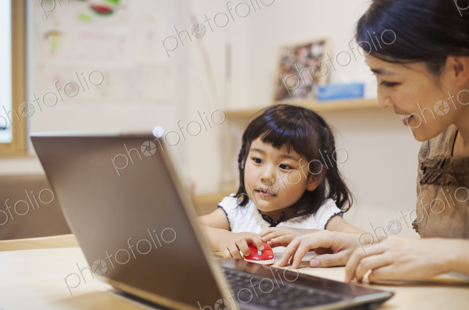 Family home. A woman and her daughter seated at a table looking at the screen of a laptop.