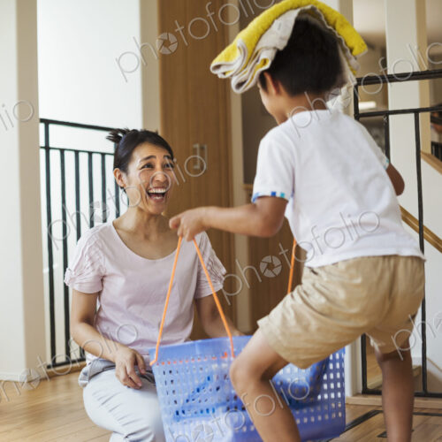 Family home. A woman and her son sorting the laundry, the boy balancing towels on his…