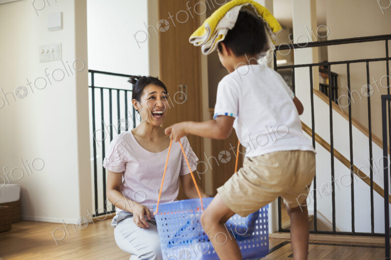 Family home. A woman and her son sorting the laundry, the boy balancing towels on his…
